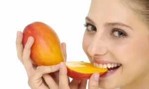 Kobieta z uśmiechem gryzie soczyste mango. Czy pies może mango? To pytanie pozostaje otwarte, ale ona na pewno je uwielbia!