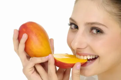 Kobieta z uśmiechem gryzie soczyste mango. Czy pies może mango? To pytanie pozostaje otwarte, ale ona na pewno je uwielbia!