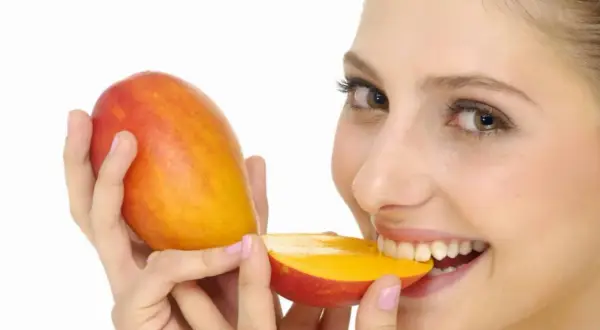 Kobieta z uśmiechem gryzie soczyste mango. Czy pies może mango? To pytanie pozostaje otwarte, ale ona na pewno je uwielbia!